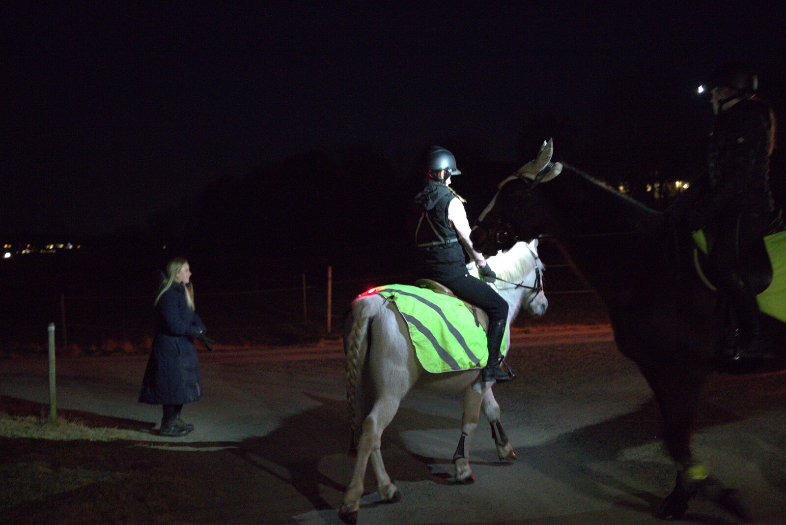 Riders on horseback at night, one wearing a hi-vis reflective rug lit by LightPlus