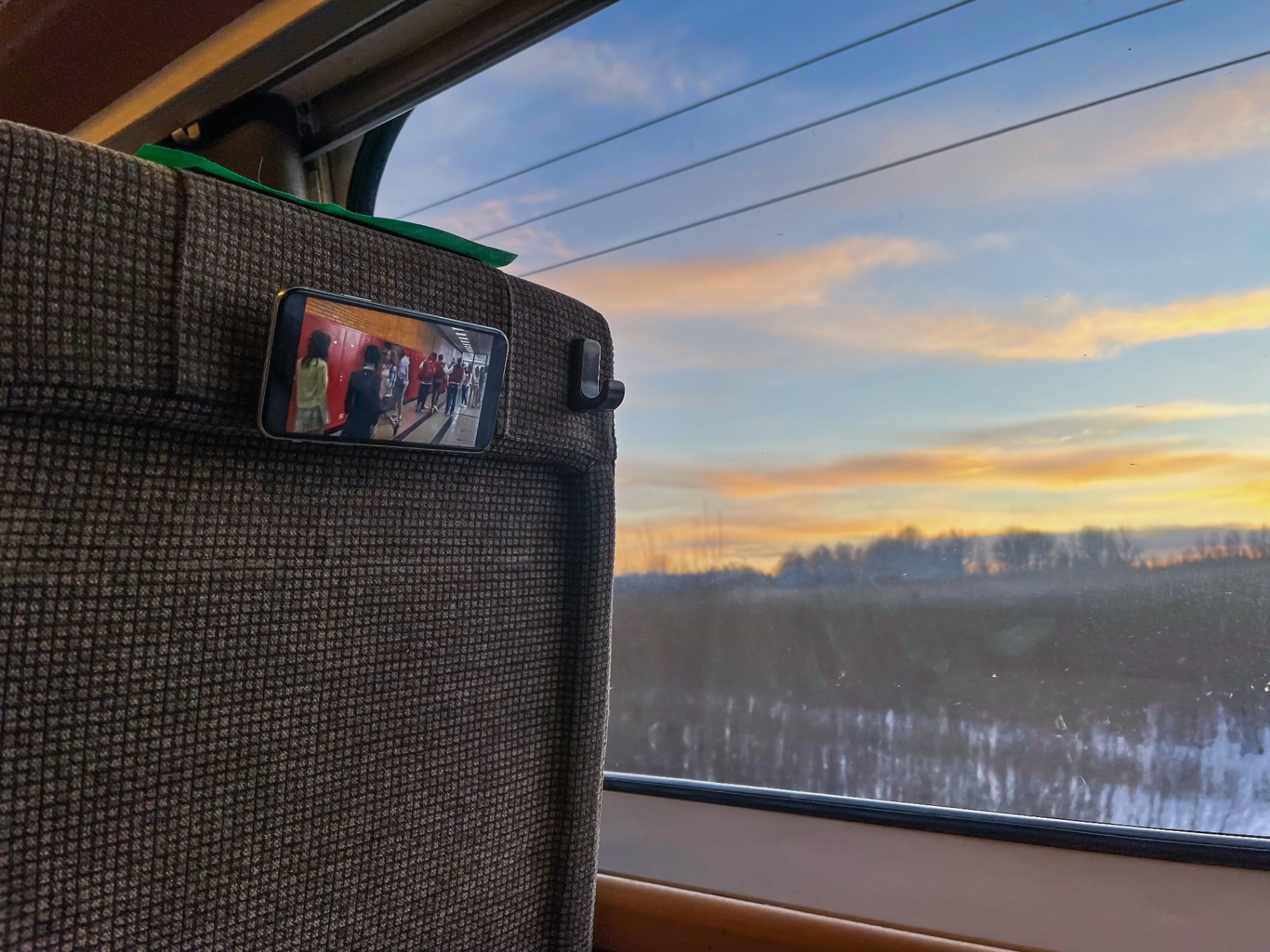 MoMag holding a phone on a train seat with a winter view